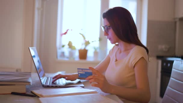 Genç bir kadın kredi kartı alışverişini yapıyor, dizüstü bilgisayar kullanıyor ve çok eğleniyor. — Stok video