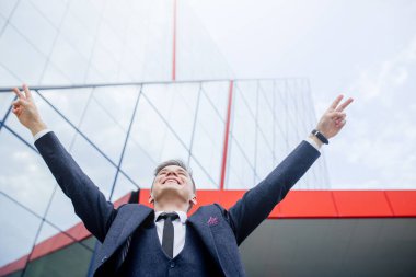 Kafkasyalı mutlu iş adamı modern ofis binasıyla çalışırken iyi haberi kutluyor.,