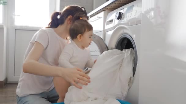 Młoda mama wziąć ubrania z pralki z dziewczynka maluch w kuchni — Wideo stockowe