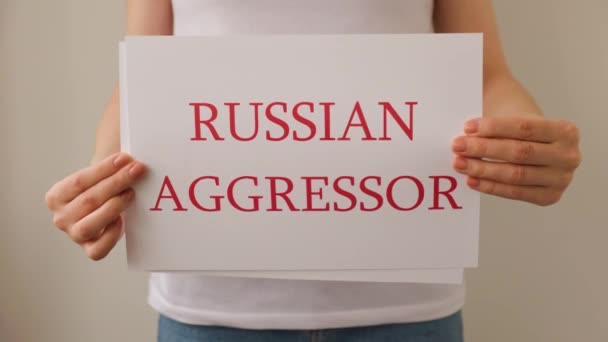 Primo piano di una mano del protestante che tiene lo stendardo di cartone con le parole aggressore russo ferma la guerra. — Video Stock