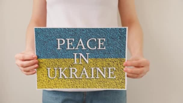Woman hands is holding a poster with the image of the Ukrainian flag, which says peace in ukraine. — Stock Video
