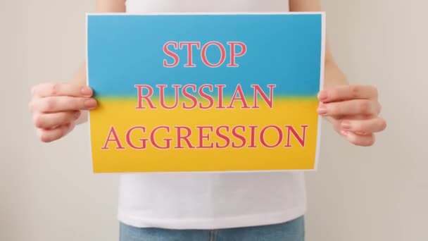 Mãos está segurando um pôster com a imagem da bandeira ucraniana, que diz parar agressão russa — Vídeo de Stock