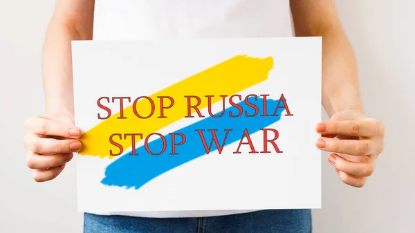 Закриття жіночих рук тримає плакат з зображенням українського прапора, який каже: "Припиніть війну, Росію!". — стокове фото