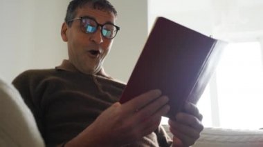 Yaşlı Hintli adam evde kitap okuyor. Gözlük takıyor. Şaşırmış bir yüzle şoktan korkuyor.