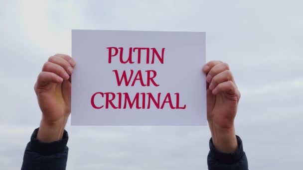 Человек держит в руках кусок белого картона со словами Putin ухо преступника — стоковое видео