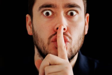 Gizemli sakallı adam kameraya bakıyor ve parmağını dudaklarına koyuyor.