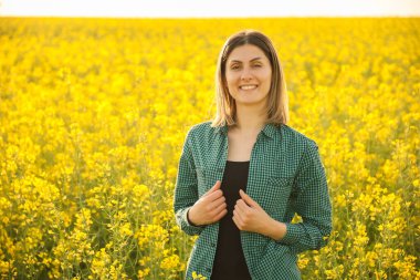 Gülümseyen çiftçi kadın sarı çiçekli kolza tohumu ve kameraya bakıyor.