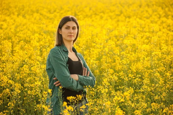 노란색 꽃피는 유채 앞에 서 있는 한 농부 가양팔을건너 카메라를 보고 있다. — 스톡 사진