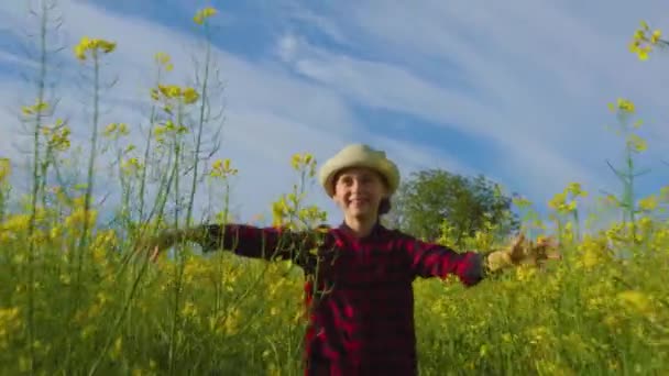Menina sorridente com cabelo loiro e chapéu olhar para câmera sorrir campo de colza — Vídeo de Stock