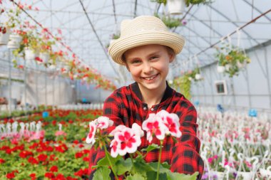 Serada çiçeklerle gülümseyen beyaz, genç bir kız çocuğu. Kameraya bakan mutlu çocuk, serada çalışmak dışında. Boşluğu kopyala