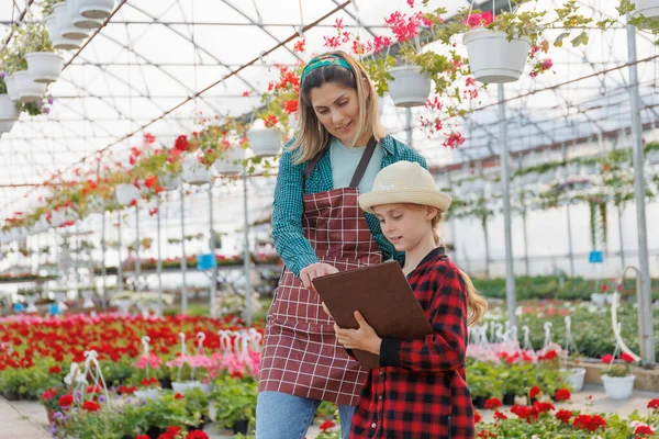 mother woman young florist helps her child to study and examine flowering in the greenhouse. familiar business of a happy family, different generations of people. copy space