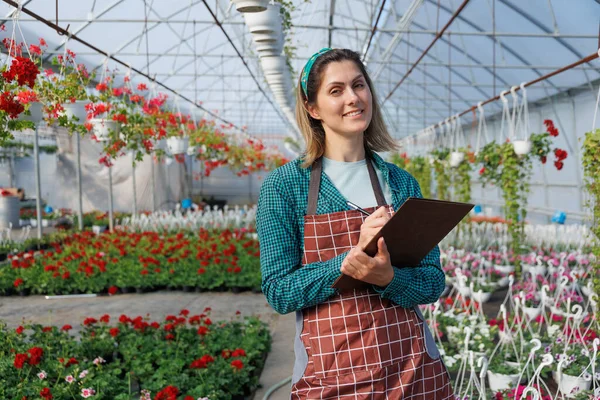 happy woman florist gardener looking at camera at work in greenhouse, copy space. Home gardening, love of flowers in glasshouse, a small woman-run business, copy space