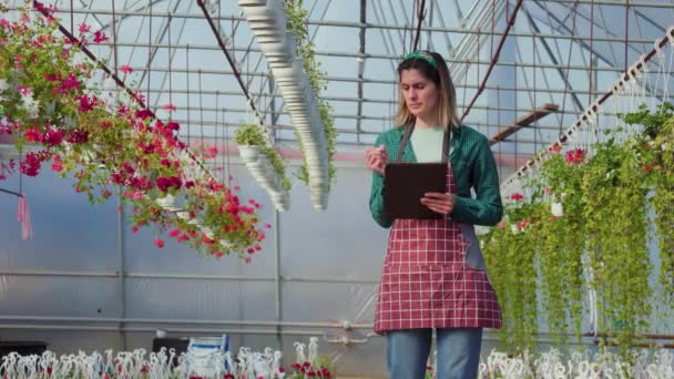 白人女性はノートを使って色の花のデータを分析し記録した温室での実験 アメリカの農業技術者が温室内の植物を検査し — ストック動画