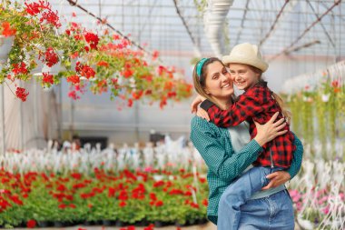 Annesinin kollarında mutlu bir çocuk, seradaki bir bahçıvan ailesi. Anne kızını sıkıca kucaklıyor. Gülümseyen anne ve küçük çocuk, kopyalama alanı