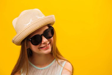 Şık, mutlu, neşeli, güneş gözlüklü, şapkalı sarışın kız çocuğu. Sarı arka planda izole edilmiş video portresi. Stüdyo. Boşluğu kopyala