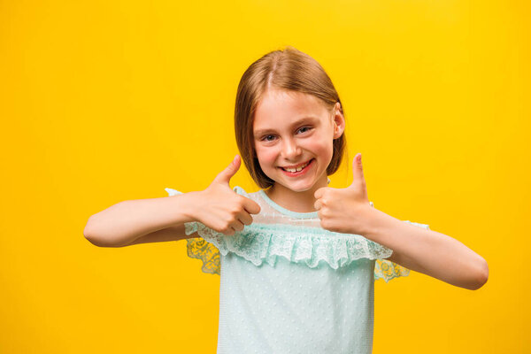 Like and approval. Studio portrait of stylish little children girl gesturing thumbs up and looking at camera. smiling to camera, yellow background