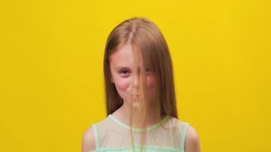 Komik kız saçlarına üflüyor ve kameraya bakıyor. Çocuk stüdyosu sarı arka planda, çocukluk eğlencesi,