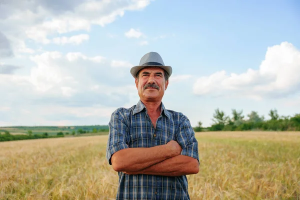 Yaşlı çiftçi bıyıklı, kolları çapraz ve şapkalı kameraya bakıp gülümsüyor. Kıdemli çiftçi mutlu, başarılı çiftçi kavramı.,