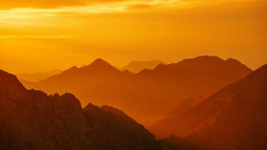 Siluetli turuncu dağlar ve Moldoveanu zirvesindeki Fagaras dağlarında ufuk çizgisi. Gün batımında dağlar, ulusal park. Gün batımında Bulutlu Gökyüzüne Karşı Dağların Manzarası