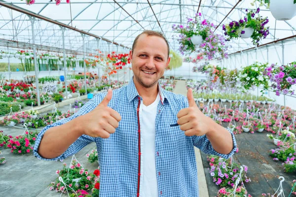 Happy Young Guy Stands Greenhouse Flowers Smiles Broadly Looking Camera — Stok fotoğraf