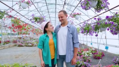 A family of aspiring flower sellers stands in a greenhouse, a boy and a girl look at each other, then turn and look at the camera. The couple is happy, with a triumphant smile on their faces. 
