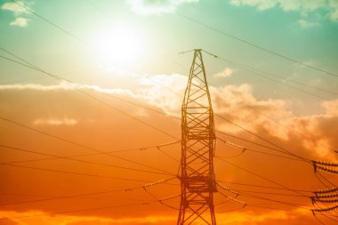 Güzel bulutlu gökyüzünün arka planında yüksek voltaj pilonu var. Elektrik Güç Hattının Silueti. Güneş, kırmızı günbatımı gökyüzünde elektrik hattı pilonunun arkasında batıyor.