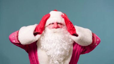 Noel Baba mavi arka planda duruyor, ellerini başının üstüne koyuyor, kırmızı eldivenler, beyaz sakal. Noel Baba tüm kış tatillerinin yoldaşıdır..