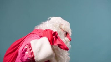 Stüdyo çekimleri mavi arka plan yorgun Noel Baba omuzlarında hediyelerle kırmızı çanta atıyor. Noel Baba ağır bir çantayı eliyle tutuyor. Peder Frost 'un yakında hediyeleri olacak..