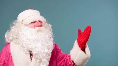 Noel Baba eldivenli elini sallayarak tek eliyle herkesi selamlıyor ve mavi arka planda sağdaki mesafeye bakıyor. Joulupukki hediye dağıtmaya ve elini sallamaya hazır. Boşluğu kopyala.