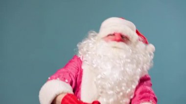 Mavi arka plan stüdyosu Noel ve yeni yıl beklentisiyle kamera dansı yapan Noel Baba 'ya bakıyor. Noel Baba, Babbo Natale, Papa Noel, Pai natal, Joulupukki, Pere noel. Boşluğu kopyala.