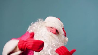 Stüdyo, neşeli Noel Baba 'yı ön planda çekti. Yarı vücut dansı, el hareketleriyle hareket ediyor. Mavi arka plan neşe ve eğlence yakında Noel ve yeni yıl.
