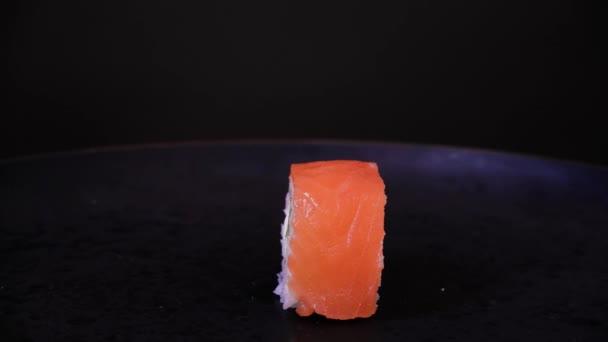 Filadelfia rotolo con pesce salmone, avocado e formaggio girare su un piatto nero su sfondo scuro. Concetto minimo — Video Stock