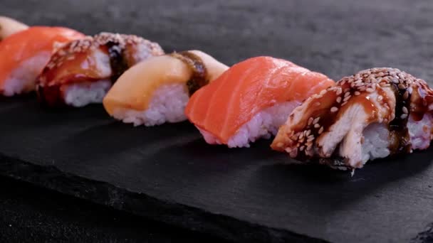 Sushi assortiti con salmone, anguilla ed escolar su un piatto nero illuminato al buio. Concetto minimo — Video Stock