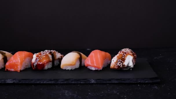 Różne sushi z łososia, węgorza i escolar przenieść na czarnej płycie na ciemnym tle. Koncepcja minimalna — Wideo stockowe
