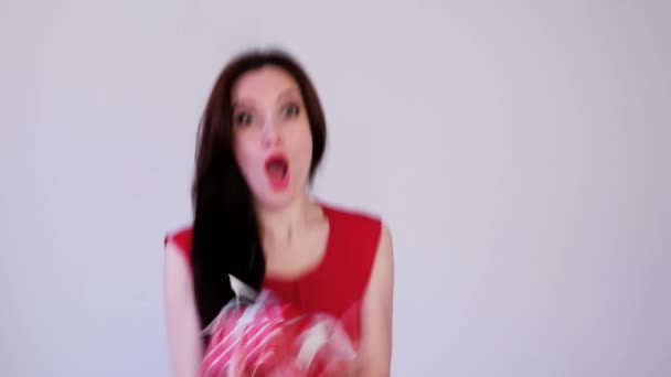 Close-up Kerst beeldmateriaal van gelukkig vrouw in rood jurk vangt een cadeau op licht achtergrond — Stockvideo