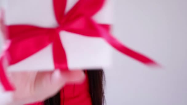 Close up Christmas footage of happy woman in red dress and Santa hat points his finger at the gift on light background — Stock Video