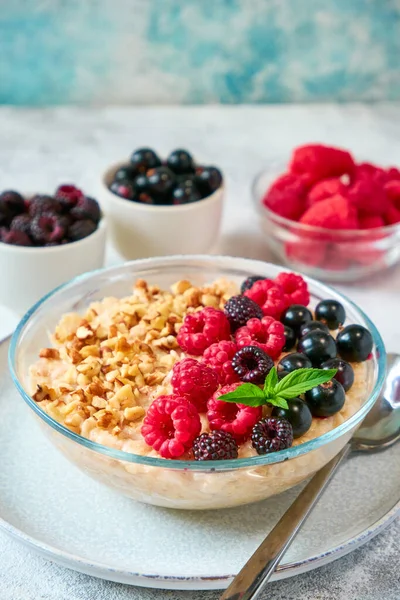 Glass bowl with oatmeal, different berries and crushed nuts in a glass bowl. Healthy balanced food.