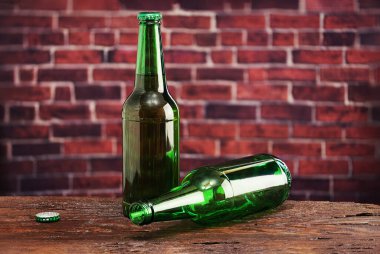 Boş bir şişe ve tuğla duvarın arkasında bir şişe bira.