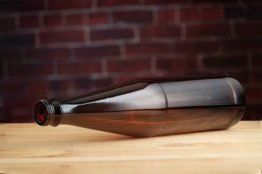 Boş bir cam bira şişesi ahşap bir masada, tuğla bir duvara karşı..
