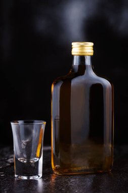 Küçük, düz, cam bir brendi şişesi ve arka planda bir shot bardağı.