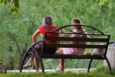 Sabah parkındaki bankta haşlanmış mısır yiyen kızlar..