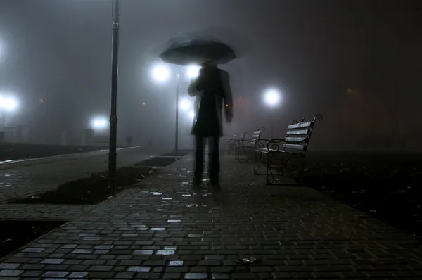 Hombre con paraguas en el parque nocturno Imagen de archivo