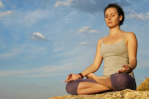 Young woman practicing yoga on the stone at the sky background — Stock Photo, Image