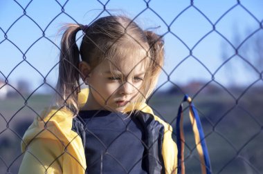 Sınırda kafes yakınında sarı ve mavi kurdeleli güzel bir Ukraynalı kızın portresi. Ukrayna 'yı kurtarmak için yardım istiyor. Savaşı durdurun..