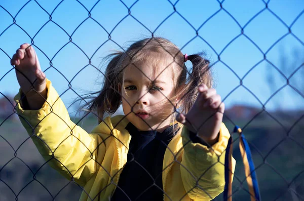 Sınırda kafes yakınında sarı ve mavi kurdeleli güzel bir Ukraynalı kızın portresi. Ukrayna 'yı kurtarmak için yardım istiyor. Savaşı durdurun..