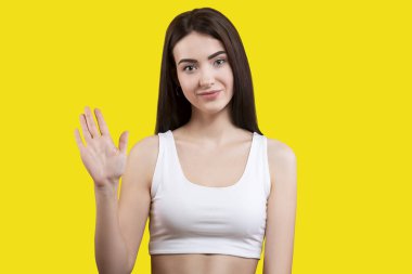 Çekici şirin kız sarı arka planda beyaz bir bluzla selam veriyor. Avuç gösterirName