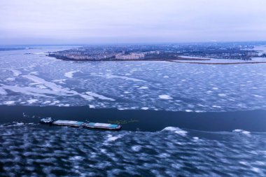 Donmuş bir nehir boyunca ilerleyen bir kargo gemisi. Nakliye konsepti, ithalat ihracat ve iş lojistiği, kışın hava manzarası.