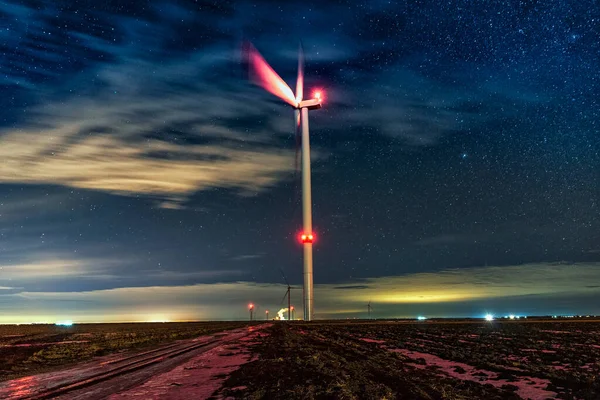Night photo of a windmill and stars with abstract lighting. Wind turbine at night against the background of stars. Environment and Renewable Energy