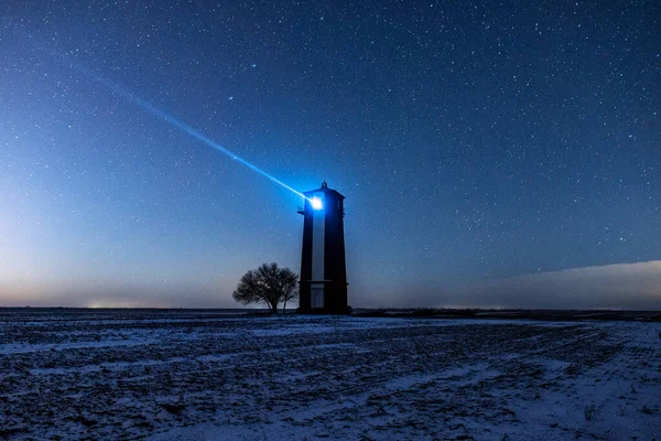 Bright lighthouse beaconing at the end of the milky way. Beautiful lighthouse. Night in the field.