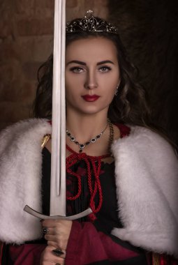Elinde kılıçla harika bir ortaçağ kadını. Kürk ve altınla saray kadifemsi kırmızı elbise, prenses kız, kraliçe, uzun saçlı esmer. Şato, alaca karanlık, lüks